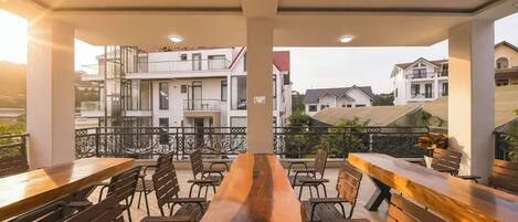 An outdoor seating area with wooden tables and chairs, overlooking a residential area with buildings.