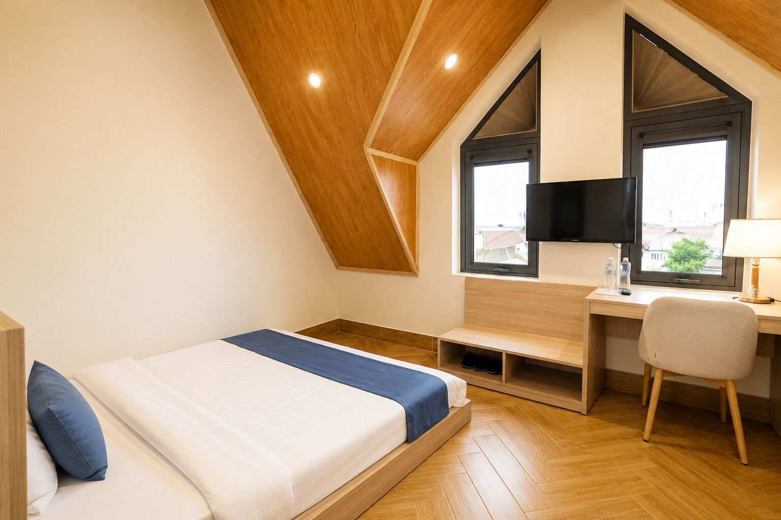 Une chambre moderne avec un plafond en pente, un lit agrémenté d’une touche de bleu, un bureau avec une chaise, un téléviseur et une fenêtre offrant une vue agréable.