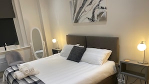 A neatly made bed with a checkered blanket, two bedside lamps, and a wall-mounted abstract painting. - Cozy Coastal Retreat in Bournemouth (Bournemouth)