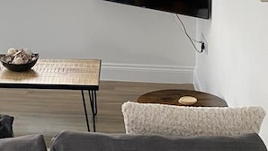 A modern living room with a flat-screen TV mounted on the wall, a round table with a bowl of eggs, and a gray sofa. - Cozy Coastal Retreat in Bournemouth (Bournemouth)