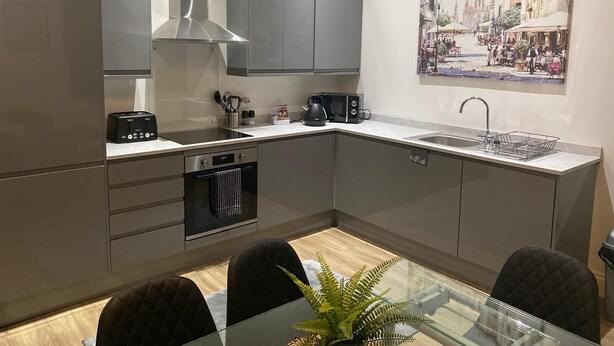 A modern kitchen with grey cabinets, a stainless steel range hood, a microwave, and a coffee maker. There's a sink with a dish rack, a dining table with chairs, and a potted plant. - Cozy Coastal Retreat in Bournemouth (Bournemouth)