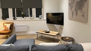 A modern living room with a large flat-screen TV, a sofa, a coffee table, and a small side table. - Cozy Coastal Retreat in Bournemouth (Bournemouth)