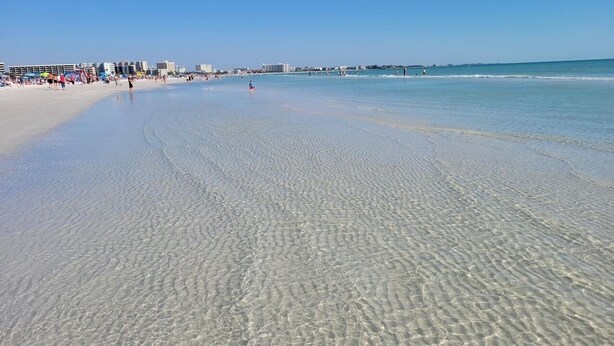 A beach with clear shallow water, a sandy shore, and buildings in the background. - Sarasota Resort Home Pool Golf Beach Siesta Key St. Armands Downtown Pickleball (Sarasota)