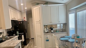 A kitchen with white cabinets, a black refrigerator, a coffee maker, and a dining area with a table and chairs. - Sarasota Resort Home Pool Golf Beach Siesta Key St. Armands Downtown Pickleball (Sarasota)