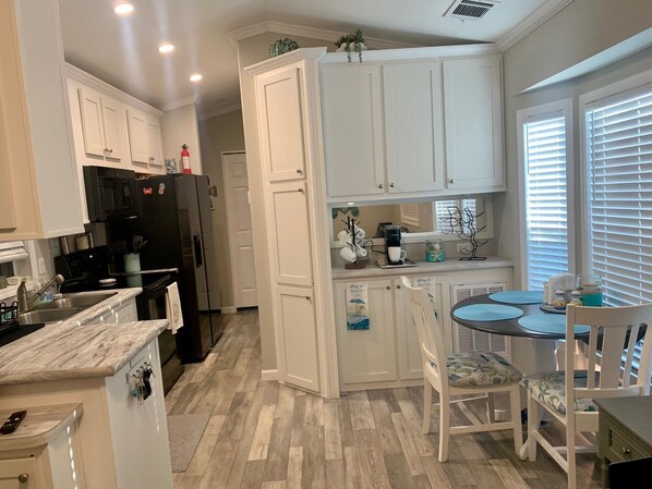 A kitchen with white cabinets, a black refrigerator, a coffee maker, and a dining area with a table and chairs.
