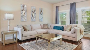 A living room with a beige sofa, a glass coffee table, and abstract wall art. - Spacious 3BR Condo in Ocean Springs (Vancleave)
