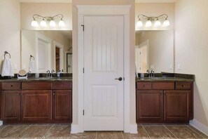 A bathroom with a double vanity, two sinks, a white door, and a mirror with light fixtures.