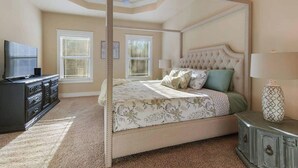 A four-poster bed with a tufted headboard, a television on a dresser, and a vase on a side table. - Spacious 3BR Condo in Ocean Springs (Vancleave)