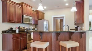 A kitchen with wooden cabinets, stainless steel appliances, and two bar stools. - Spacious 3BR Condo in Ocean Springs (Vancleave)