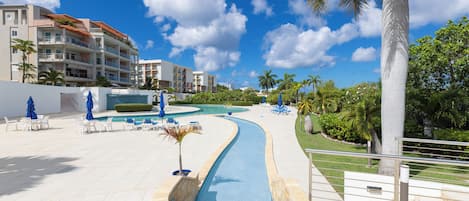 Un área de piscina en un resort con una fuente curva, sillones de descanso y palmeras.