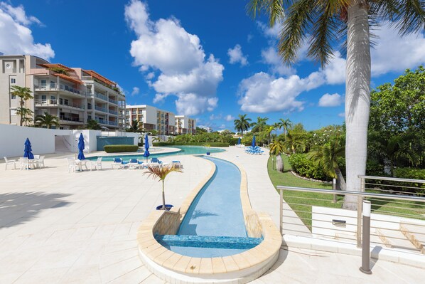 Un área de piscina en un resort con una fuente curva, sillones de descanso y palmeras.