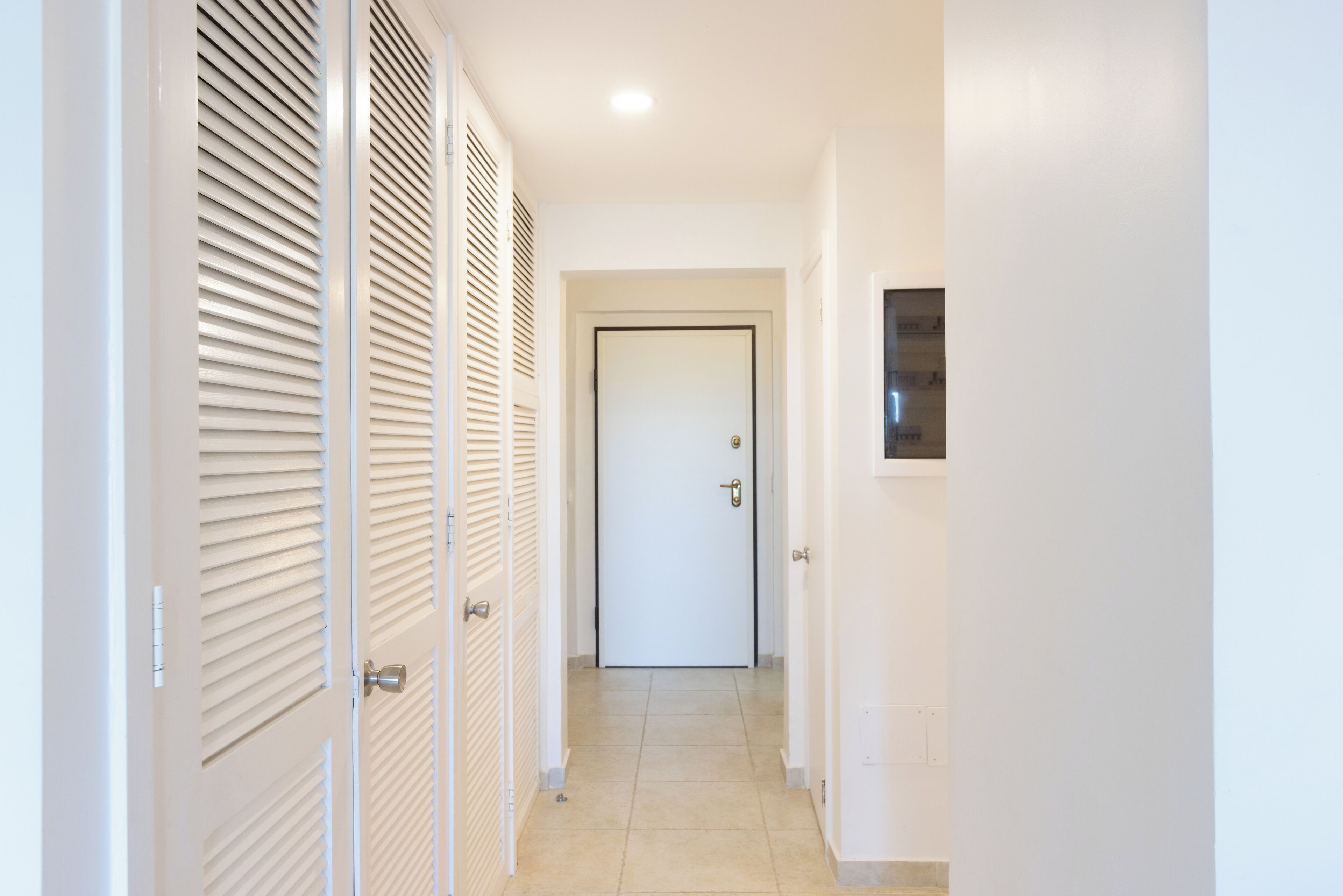 A hallway with a white door at the end, leading to a room.