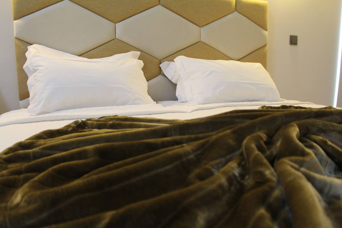 A bed with white pillows and a dark brown blanket, set against a headboard with a geometric pattern.