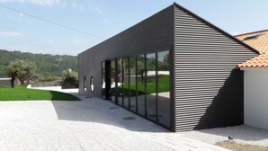 A modern building with a sloped roof, large glass windows, and a gravel driveway. - Hostel Pia do Urso (Batalha)