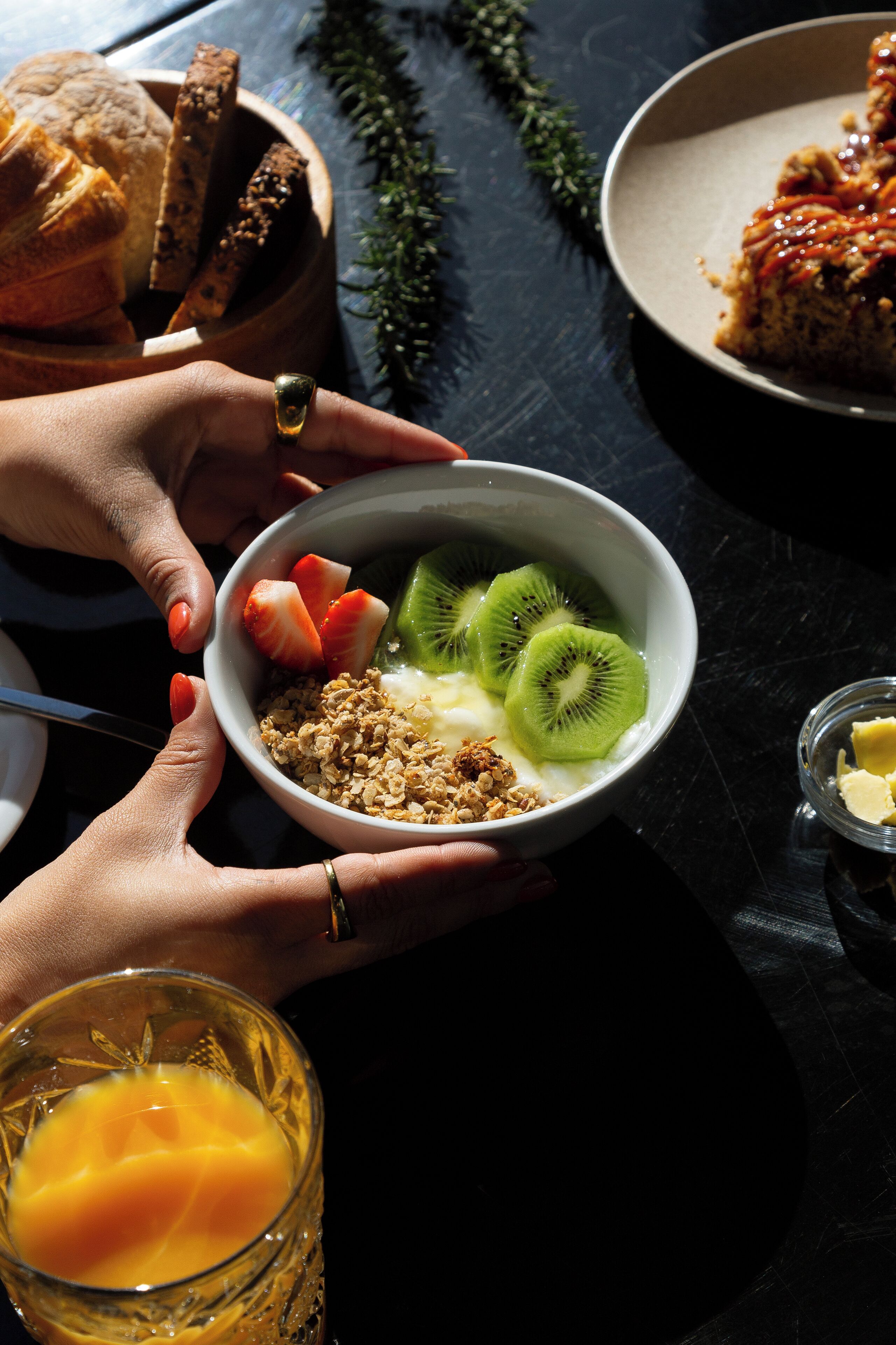 A bowl of cereal with fruits and a glass of orange juice on a table.