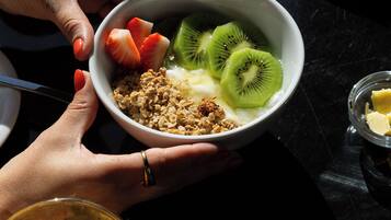 A bowl of cereal with fruits and a glass of orange juice on a table.