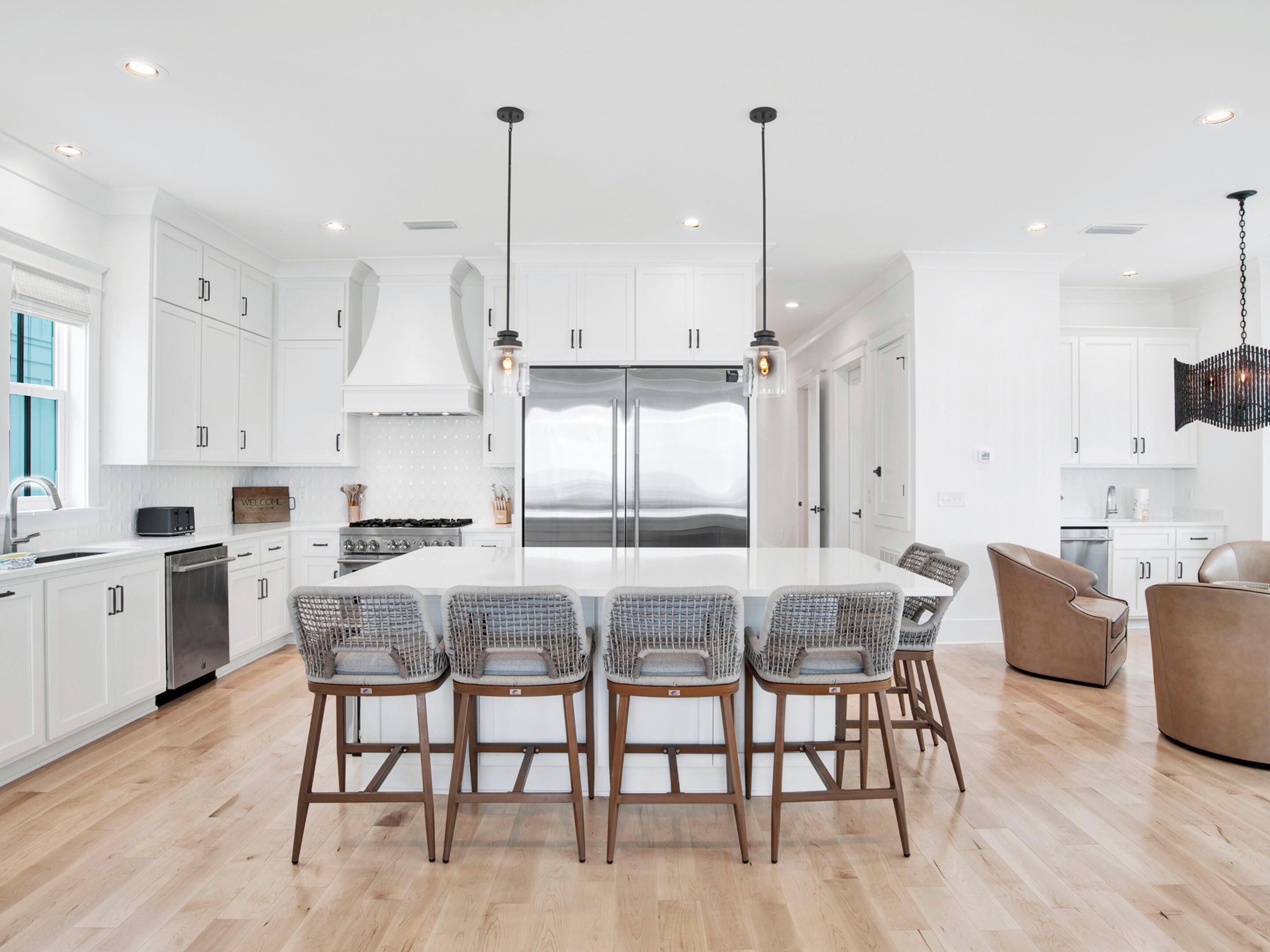 A modern kitchen with white cabinetry, a central island with bar stools, stainless steel appliances, and pendant lighting.