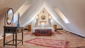 A bedroom with a bed, a mirror, a dresser, and a red rug in a loft-style room with sloped ceilings and brick flooring. - Dominic Boutique  (Saschiz)