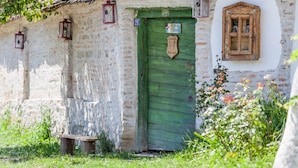 A rustic building with a green door, a small bench, and a window with a wooden shutter. - Dominic Boutique  (Saschiz)