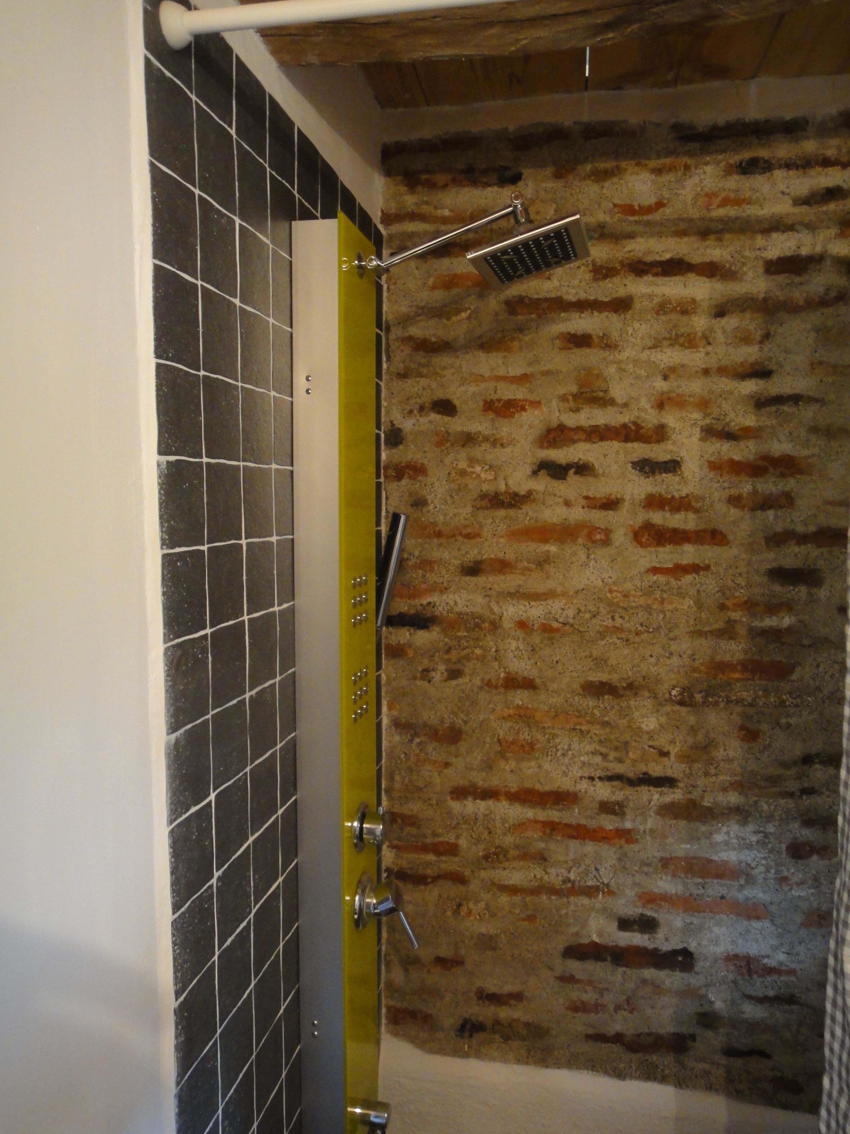 Un baño con pared de azulejos, un perchero amarillo y un cabezal de ducha.