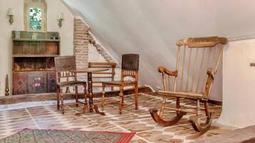 A room with a wooden rocking chair, a wooden table, a bench, and a patterned rug on a tiled floor.