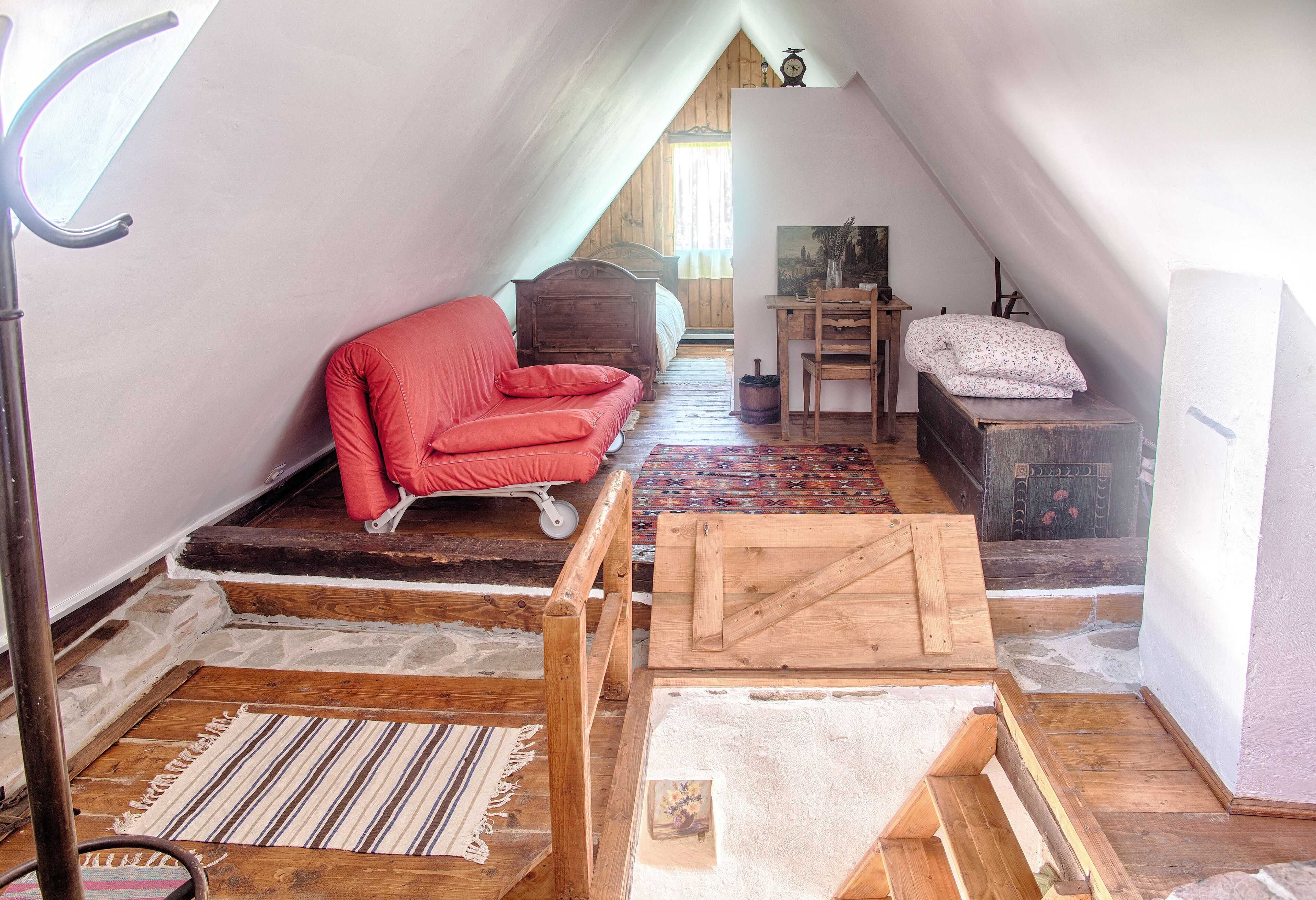 Un dormitorio tipo loft con techo inclinado, una silla roja, una cama de madera, un escritorio pequeño y un tapete estampado.