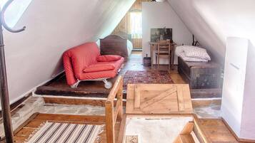 Un dormitorio tipo loft con techo inclinado, una silla roja, una cama de madera, un escritorio pequeño y un tapete estampado.