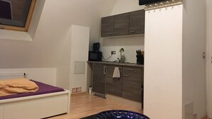 Ein kleines Zimmer mit Bett, einer Küchenzeile und einem wandmontierten Fernseher.