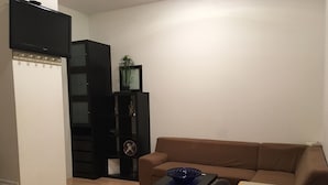Ein Wohnzimmer mit einem braunen Sofa, einem kleinen Tisch mit einer blauen Schale, einer schwarzen Unterhaltungsanlage und einer weißen Wand.