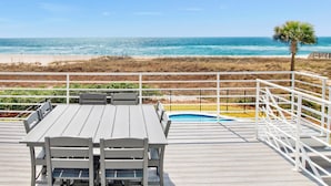 Une terrasse en bois avec une table et des chaises, donnant sur une plage et une piscine.