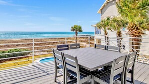 Une terrasse en bois avec une table et des chaises, donnant sur une plage et l’océan.