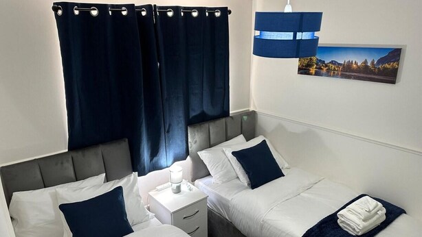 A hotel room with two beds, a nightstand, a lamp, a curtain, and a painting on the wall.