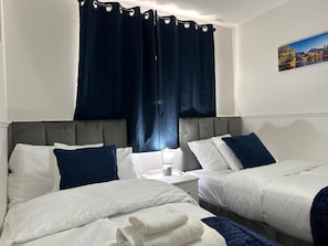 A hotel room with two beds, a nightstand, a lamp, and a painting on the wall. - House Sleeps 7 - Contractors, Free Parking (Wigan)