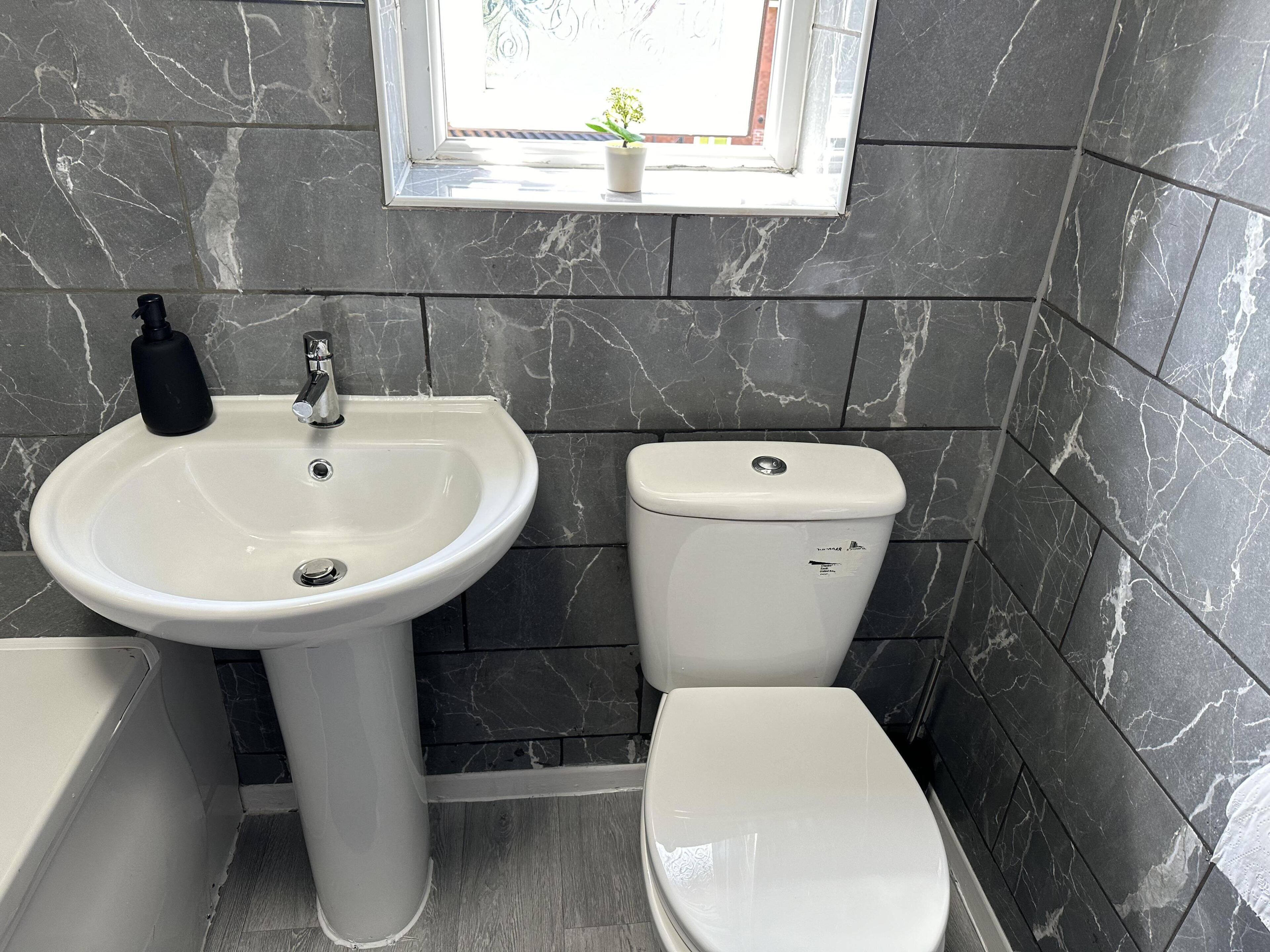 Une salle de bain avec un lavabo blanc, des toilettes et une fenêtre donnant sur l’extérieur.