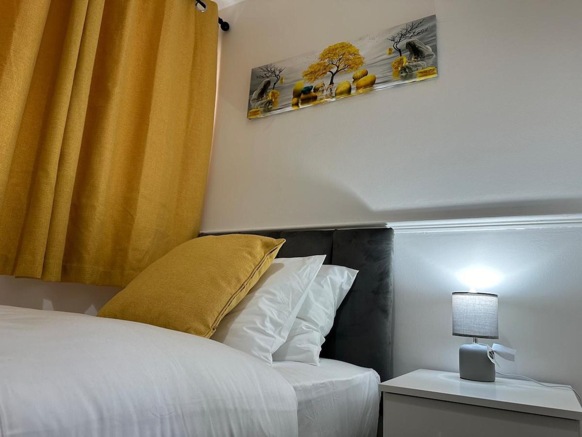 Een hotelkamer met een bed, nachtkastje, lamp en een schilderij aan de muur.