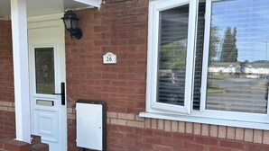 A brick house with a white door, a window with blinds, and a number '26' on the wall.