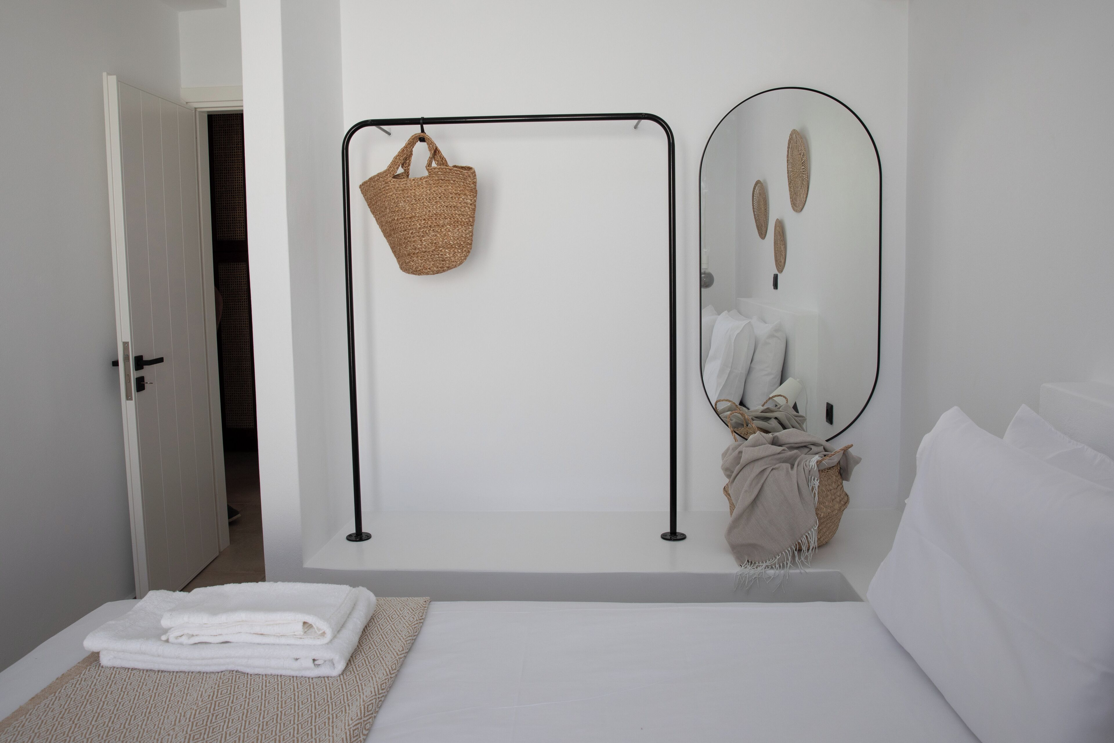 A bedroom with a bed, a bedside table, a hanging basket, a mirror, and a door leading to a bathroom.