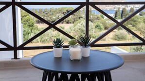 A round table with three potted plants and a candle on a balcony with a view of greenery and buildings. - Serenity Bay, Cycladic Villa with Pool and magnificent view near the beach. (Leros)