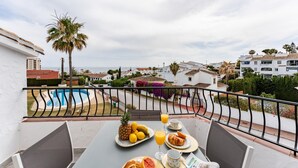Balkon med et morgenmadsbord, der giver udsigt over en swimmingpool og et boligområde.
