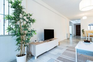 Un salon moderne avec un téléviseur à écran plat posé sur un meuble blanc, une grande plante en pot et un tapis à motifs.