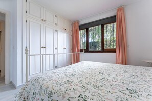 Une chambre avec un grand lit, une armoire blanche et une fenêtre avec des rideaux.