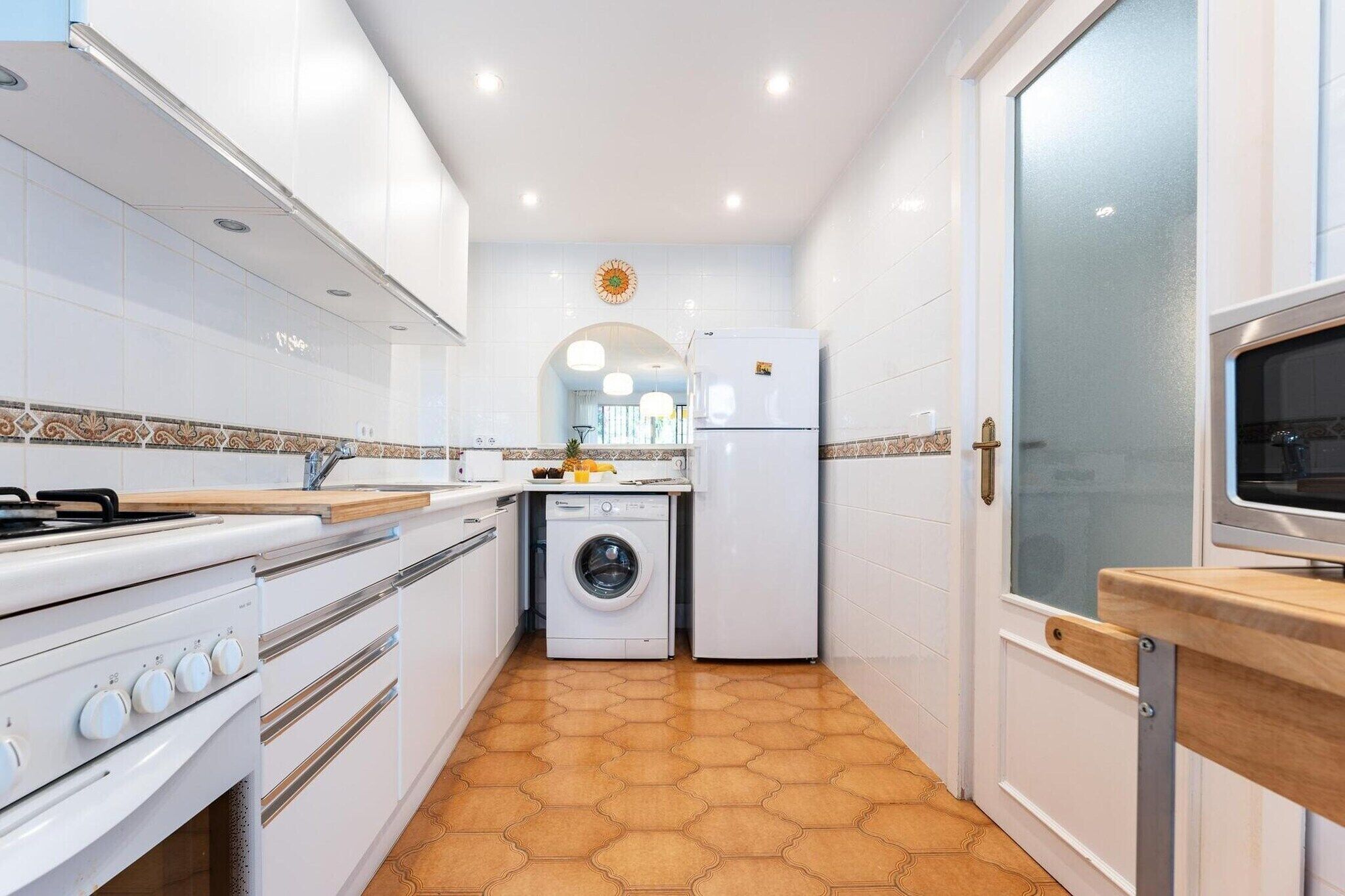 A compact kitchen with a stove, sink, washing machine, and a microwave.