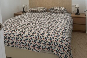 A bed with a patterned bedspread, two bedside tables with lamps, and a wooden headboard. - Faro's Retamar Cuddly Nest for 2 (Almería)
