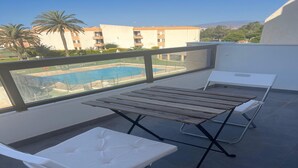 A balcony with a pool view, a table, and two lounge chairs. - Faro's Retamar Cuddly Nest for 2 (Almería)
