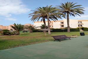 A courtyard with palm trees, a bench, and a building with balconies in the background. - Faro's Retamar Cuddly Nest for 2 (Almería)