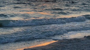 Een zonsondergang boven de oceaan met golven die op het strand breken.