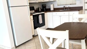 Een keuken met witte kastjes, een koelkast, een magnetron, een fornuis en een eettafel met stoelen.