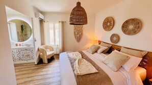 Een slaapkamer met een bed, een stoel, een nachtkastje, een lamp en een decoratief object aan de muur.