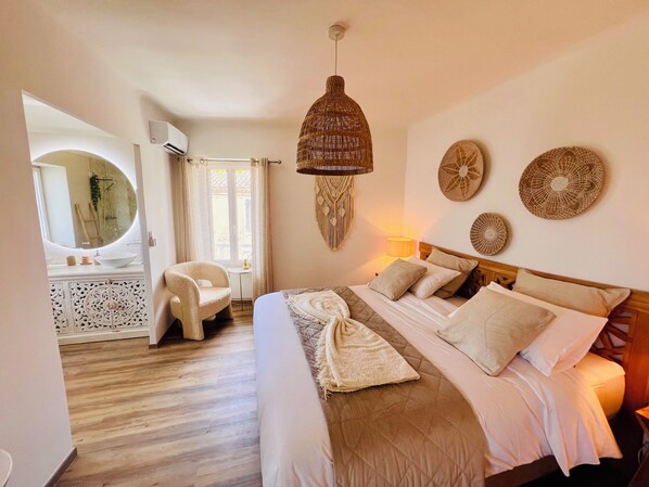 Quarto com cama, cadeira, mesa de cabeceira, luminária e um objeto decorativo na parede.
