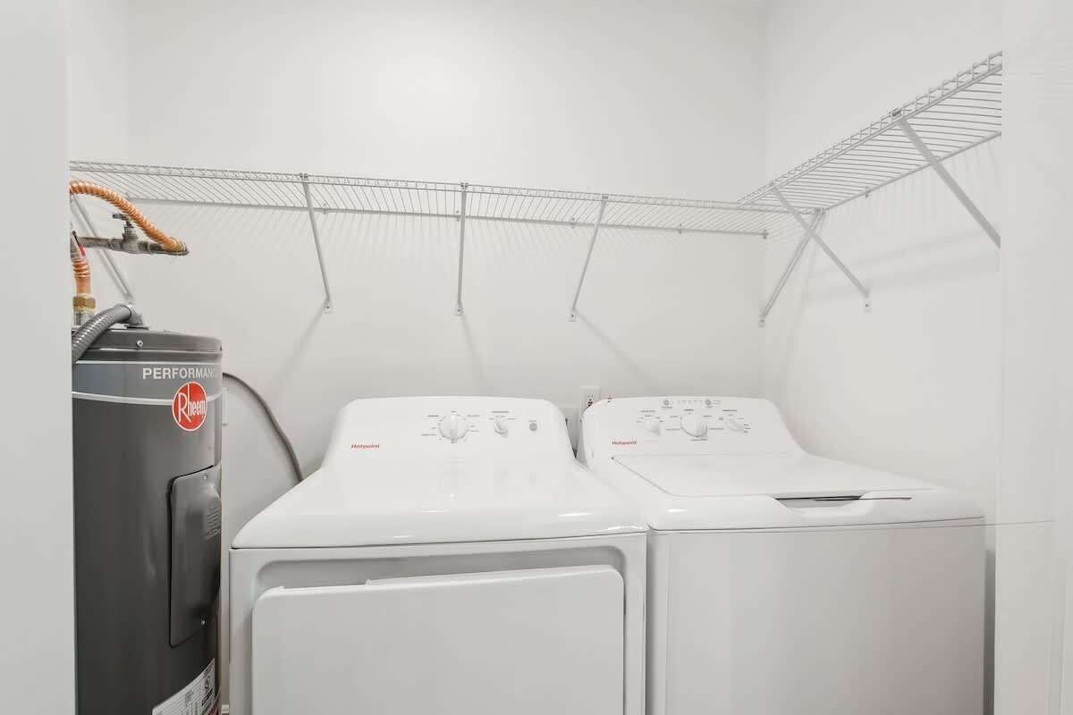 A laundry room with two white washers and a dryer, a metal drying rack, and a vacuum cleaner.